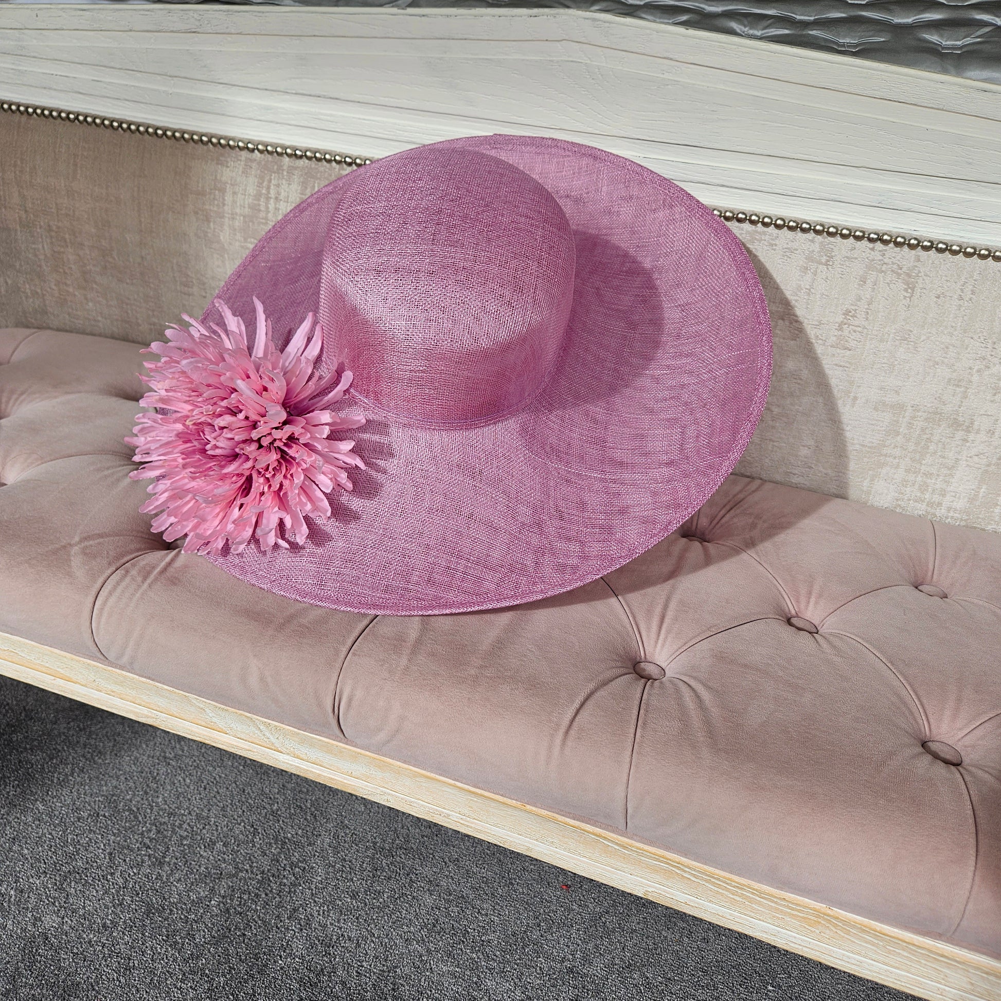 A wide-brimmed large pink at with a flower for women to wear at horse races, weddings, garden parties