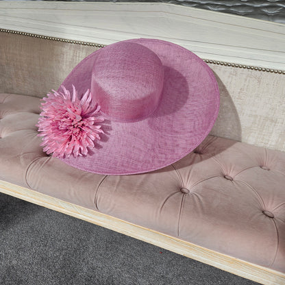 A wide-brimmed large pink at with a flower for women to wear at horse races, weddings, garden parties